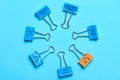 Smiley metal binder clips colored blue and yellow laid out in a circleÃÂ on turquoise background. Yellow paper clip differs from